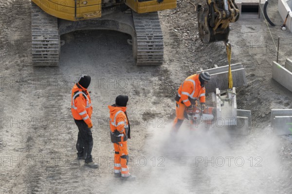 Construction workers in protective clothing work with machines on a dusty construction site,