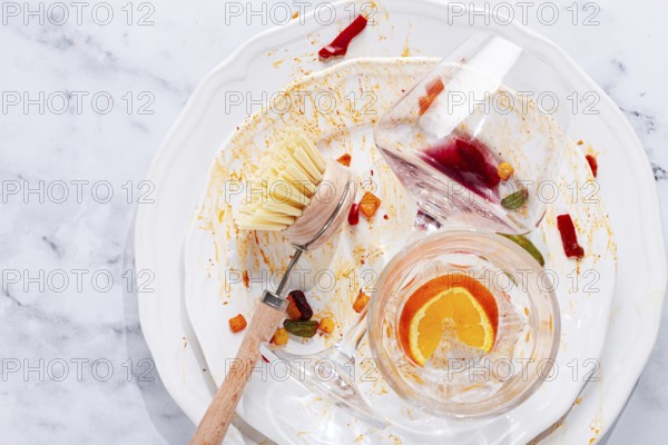 Dishes are stacked on a kitchen counter with food remnants after a meal. A cleaning brush and