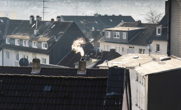 Smoke plume from a chimney over densely built residential area in the evening light, wintry city
