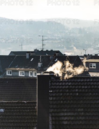 Smoke plume from a chimney over densely built residential area in the evening light, wintry city
