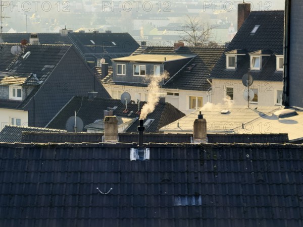 Smoke plume from a chimney over densely built residential area in the evening light, wintry city