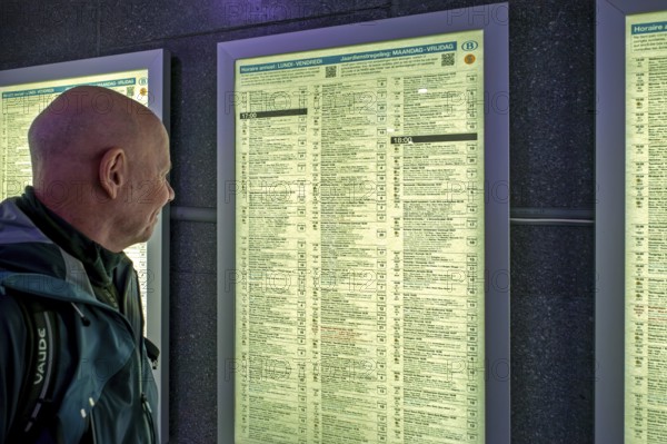 Traveler, commuter looking at train departures in timetable of NMBS Brussels-South railway station,