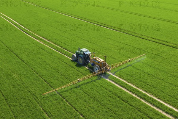 Aerial view over agricultural trailed field sprayer pulled by tractor spraying crop on farmland,