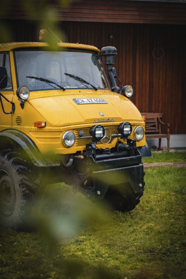 Yellow Unimog in the rain next to a wooden building in a meadow, tree work, Gechingen, Calw