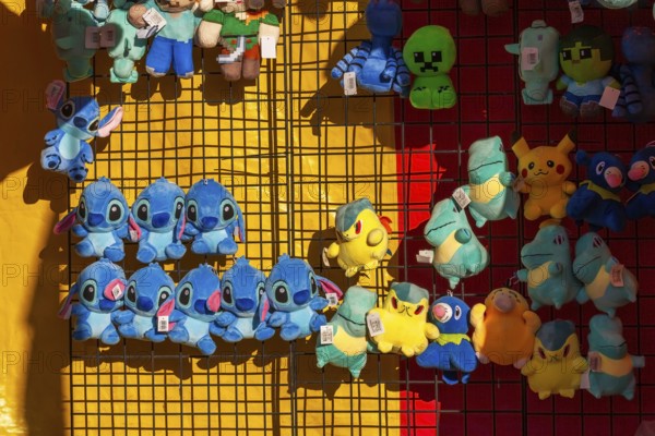 Close-up of blue, yellow and green plush prize dolls at game kiosk at Fun Show traveling ride park,