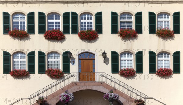 Architectural façade with symmetrical windows and green shutters decorated with red flowers, Bad