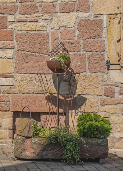 Rustic iron decoration on a stone wall, clay pot with plants in sunshine, Palatinate,
