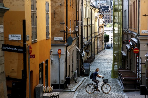 A cyclist in a picturesque old town alleyway in Stockholm, surrounded by charming buildings,