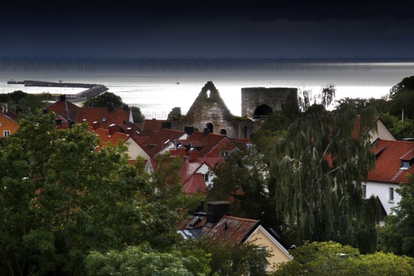 View of Visby's old town with red roofs and church ruins, surrounded by lush greenery and sea