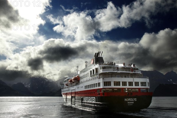 Hurtigruten ship sails through Øksfjord under cloudy sky, Øksfjord, Norway