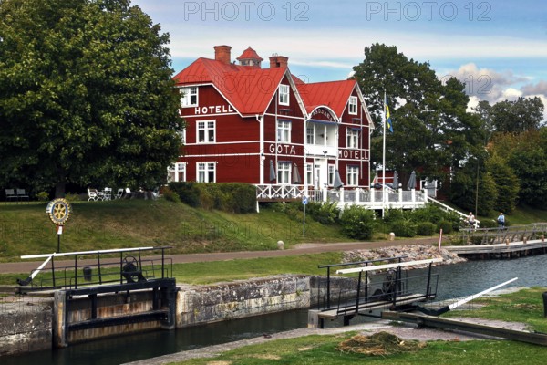 Red Göta Hotel in Borensberg on the Göta Canal next to a lock, surrounded by green trees,