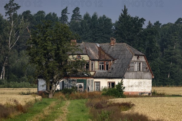 Abandoned house surrounded by fields and trees under cloudy sky, Zemgale, Latvia