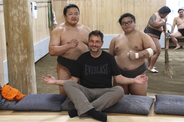 Man sitting smiling in front of two sumo wrestlers at Ryogoku training center, Tokyo, Ryogoku,