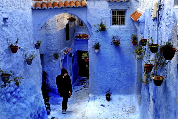 Blue alley with arches and flower pots interspersed with a passing person in the Medina,