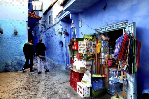Market stand on a blue wall in the medina of Chefchaouen, people strolling, Chefchaouen, Morocco