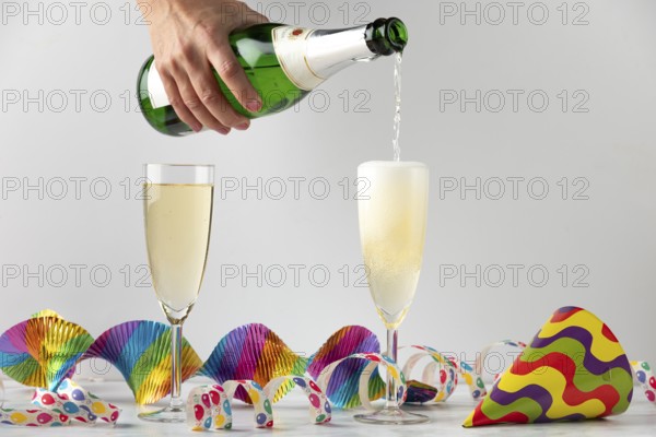 Sparkling wine is filled into glasses surrounded by colorful streamers, carnival