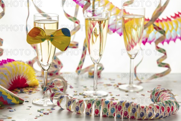 Three champagne glasses decorated with bows, surrounded by colorful confetti and streamers,