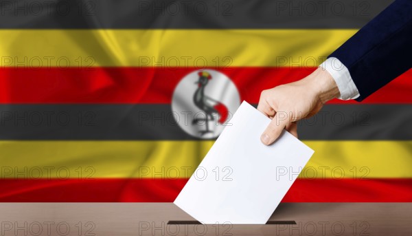 Uganda presidential vote 2026. Hand placing a ballot in ballot box with the Ugandan flag in the