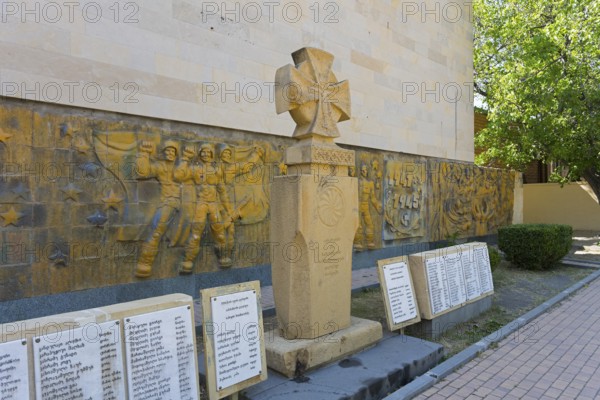 Monument with artistic relief surrounded by memorial plaques in shady surroundings, monument in