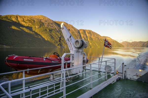 Red lifeboat and Norwegian flag on a ferry in the Lysefjord at sunset, view from the Columbus