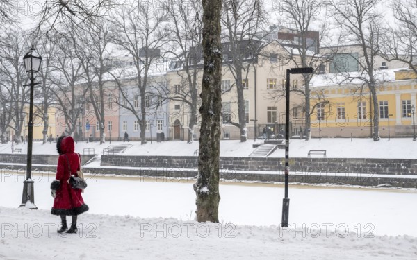Woman in red winter coat walks along the frozen Aurajoki river, wintery Turku or Swedish Åbo,
