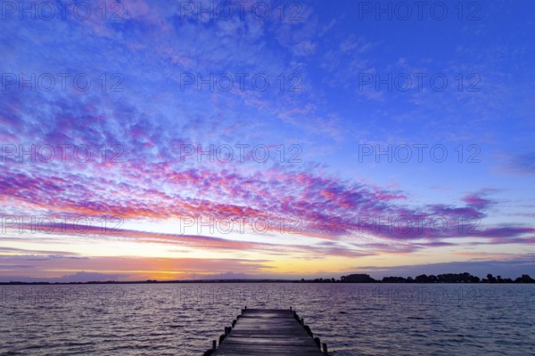 A footbridge leads into Lake Dümmer, above it a colorful sky at sunset, Dümmer nature park Park,