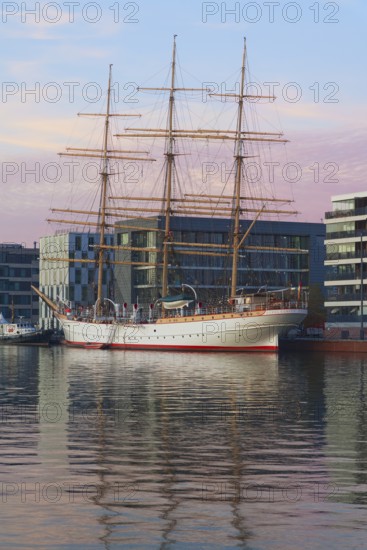Large sailing ship in harbor in front of modern buildings at dusk