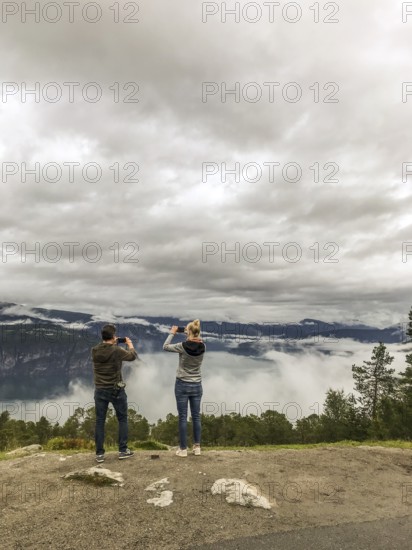 Utvik, Vestland, Norway, Two people photograph a foggy landscape with mountains and clouds with