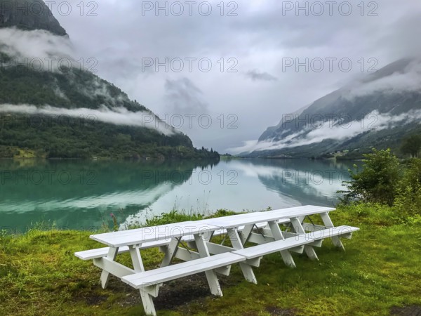 Olden, Vestland, Norway, white picnic table at a lake with mountains and low-hanging clouds in the
