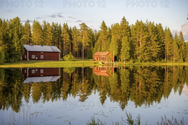 Östanå, Torsby, Värmland, Sweden, Two red buildings by the lake, perfectly reflected in calm water,