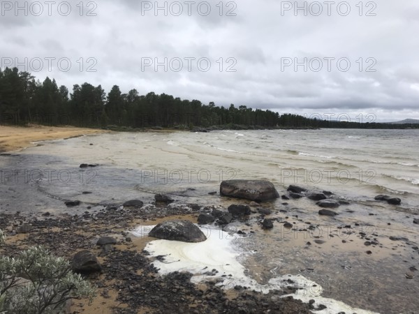 Drevsjø, Innlandet, Norway, A grey beach day with wavy water of Lake Femund, rocks and a thick