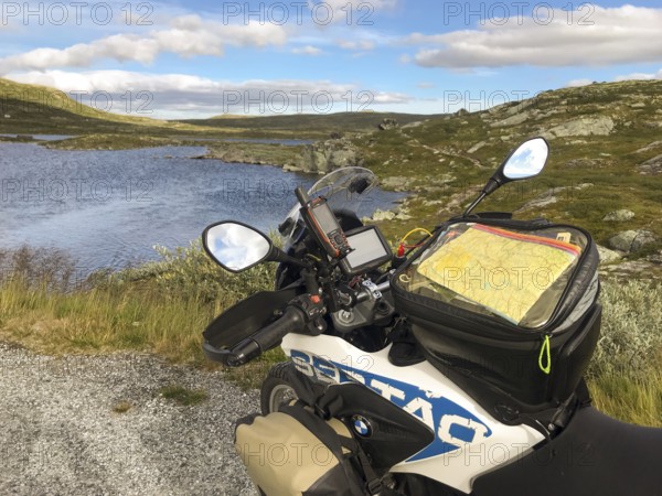 Haugastøl, Viken, Norway, A motorcycle with a map overlooks a quiet seascape in Hardangervidda