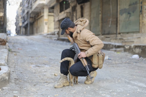 In Aleppo, Syria on January 10, 2026, a Syrian Army soldier crouches to pet a stray cat in the