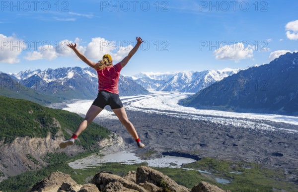 Young woman jumping into the air, view of impressive mountain landscape with Matanuska glacier and