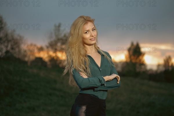 Cheerful woman with blonde hair stands with her arms crossed on a heel during sunset. Retreat in a