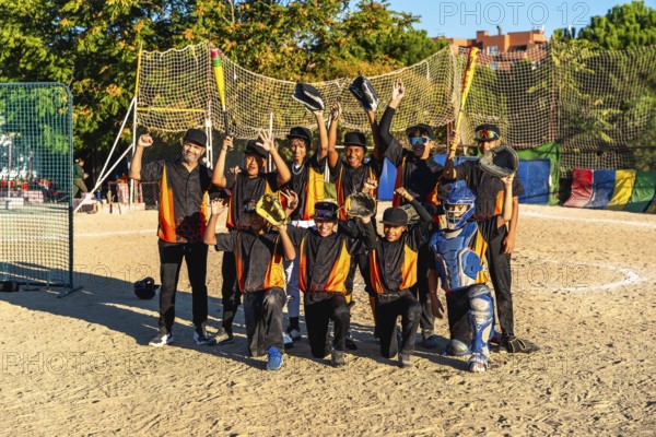 Young baseball team and coach standing together on an outdoor dirt field, raising bats and gloves