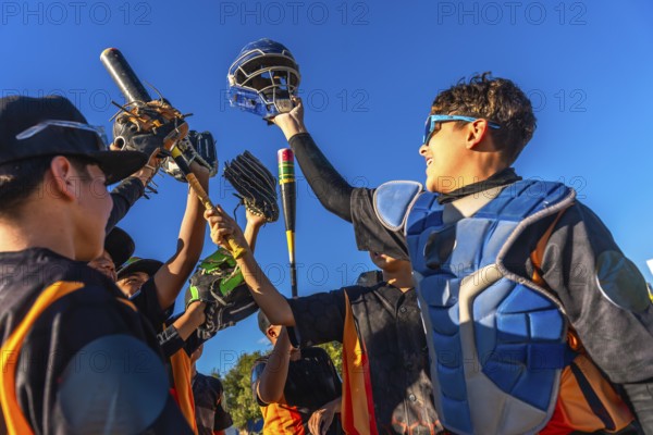 Young baseball team members cheering together, raising bats, gloves, and a catcher's helmet into