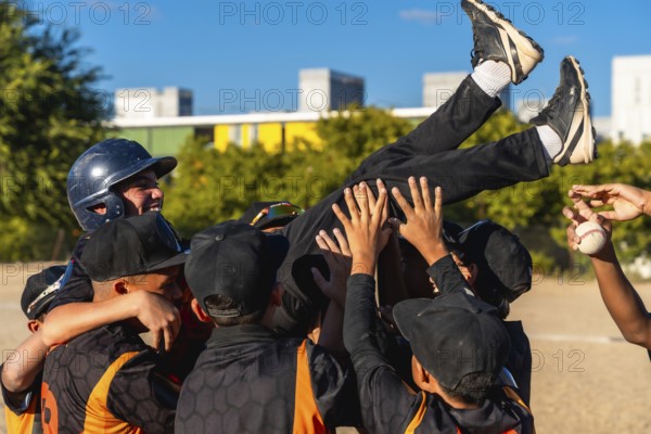 Young baseball teammates lift a smiling boy in celebration after a game, sharing joyful camaraderie