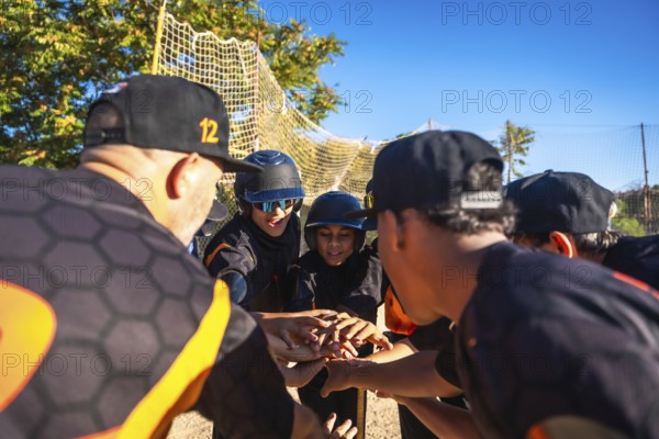 Baseball coach and diverse youth team link hands in a motivating pre game huddle on a sunny field,