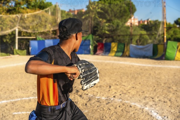 Young boy playing baseball, wearing a glove and cap, holding a ball, practicing pitching on a dirt