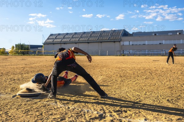 Baseball player sliding into home plate in a cloud of dust, attempting to score as the catcher