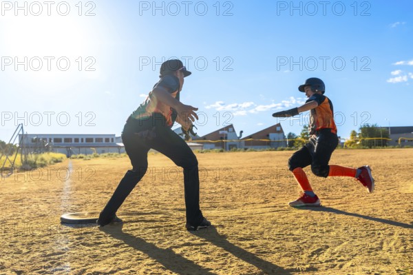 Youth baseball player sprinting hard across the dirt toward a base while coach or teammate awaits,
