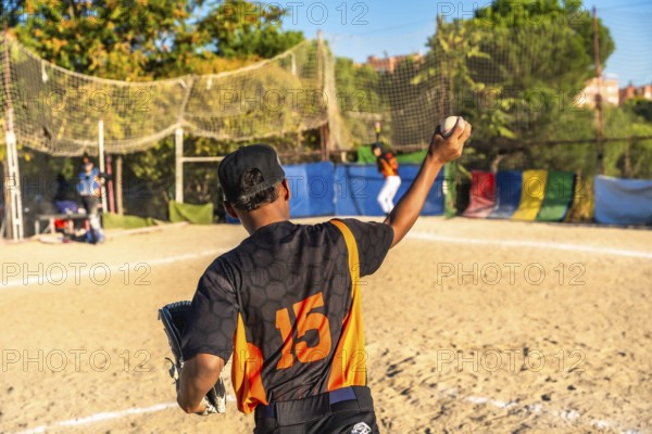 Young baseball pitcher in a black and orange uniform with number 15 on the back holding a ball