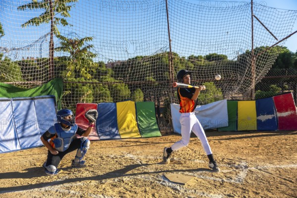 Young baseball players focusing on sport, with a batter hitting a baseball and a catcher ready
