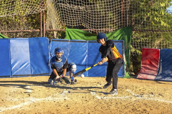 Youth baseball players, a batter taking a swing at a pitch and a catcher ready behind home plate,