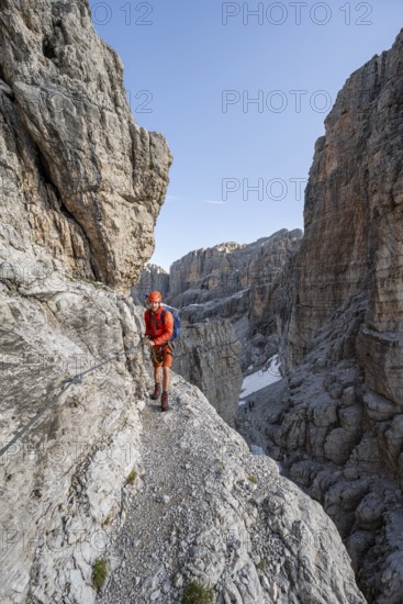 Mountaineer climbs an exposed rock band in the secured via ferrata Bocciere Centrale, Brenta