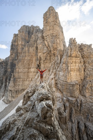 Mountaineer stretches his arms in the air, climbs an exposed rock in the secured Via Ferrata