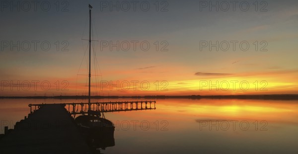Tranquil Dümmer See with dock and sailboat at sunset, warm colors and calm atmosphere, Lembruch,