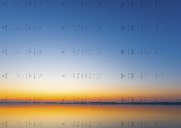 A calm sunrise with a soft color gradient is reflected in the still water of Lake Ddümmer, Dümmer