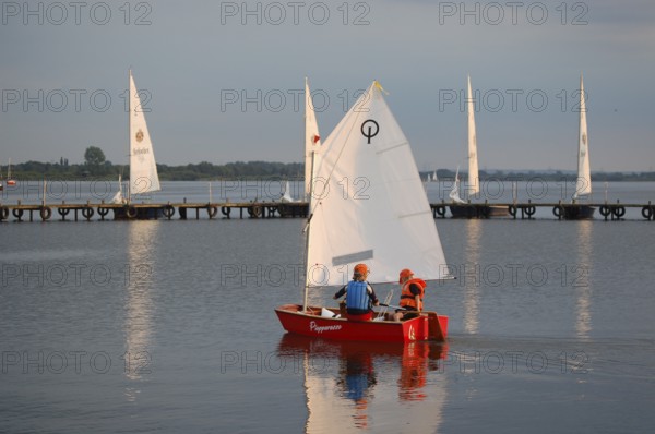 Two children 6 and 10 years old in a small red sailboat Optimist Jolle Opti on Lake Dümmer in calm